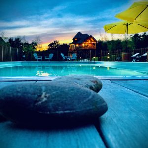 Cabane perchée en Aquitaine, vue sur la piscine et parasols jaunes au coucher de soleil.
