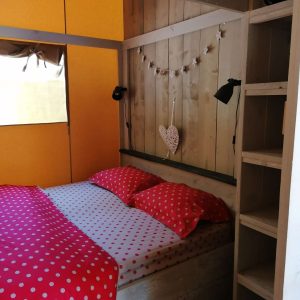 Chambre en bois avec lit à baldaquin, draps à pois rouges, ambiance chaleureuse.