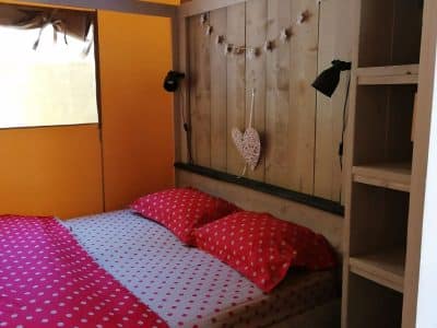 Chambre en bois avec lit à baldaquin, draps à pois rouges, ambiance chaleureuse.