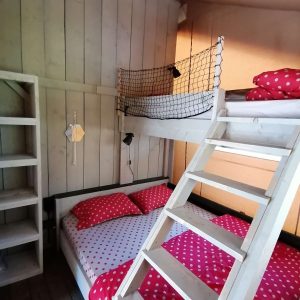 Chambre en cabane avec lits superposés et draps à pois rouges, ambiance cosy.