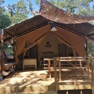 Tente safari en bois, avec terrasse ensoleillée et décor naturel au Languedoc-Roussillon.