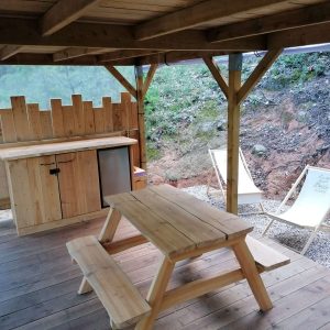 Cabane en bois avec coin repas et chaises longues, au cœur de la nature.