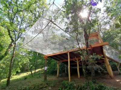 Cabane perchée dans les arbres, entourée de verdure et protégée par un filet.