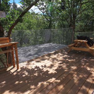 Cabane perchée dans les arbres, avec terrasse en bois et vue sur la nature verdoyante.