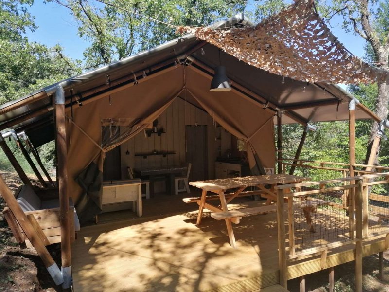 Tente safari spacieuse en bois, avec terrasse et mobilier extérieur en pleine nature.