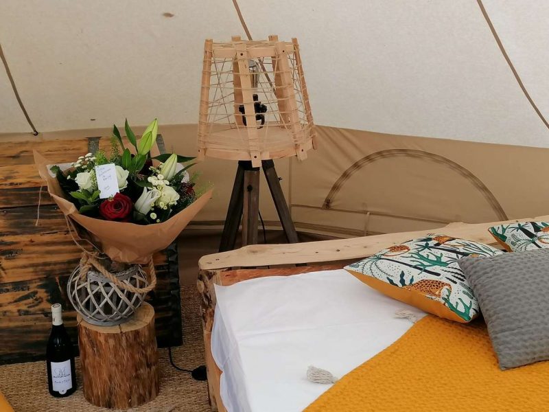 Tente glamping élégante avec lit douillet, fleurs et bouteille de vin.