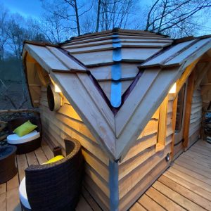 Cabane en bois perchée, toit en pente, avec terrasse et fauteuils confortables.