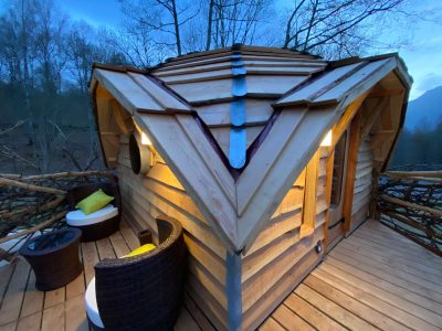 Cabane en bois perchée, toit en pente, avec terrasse et fauteuils confortables.