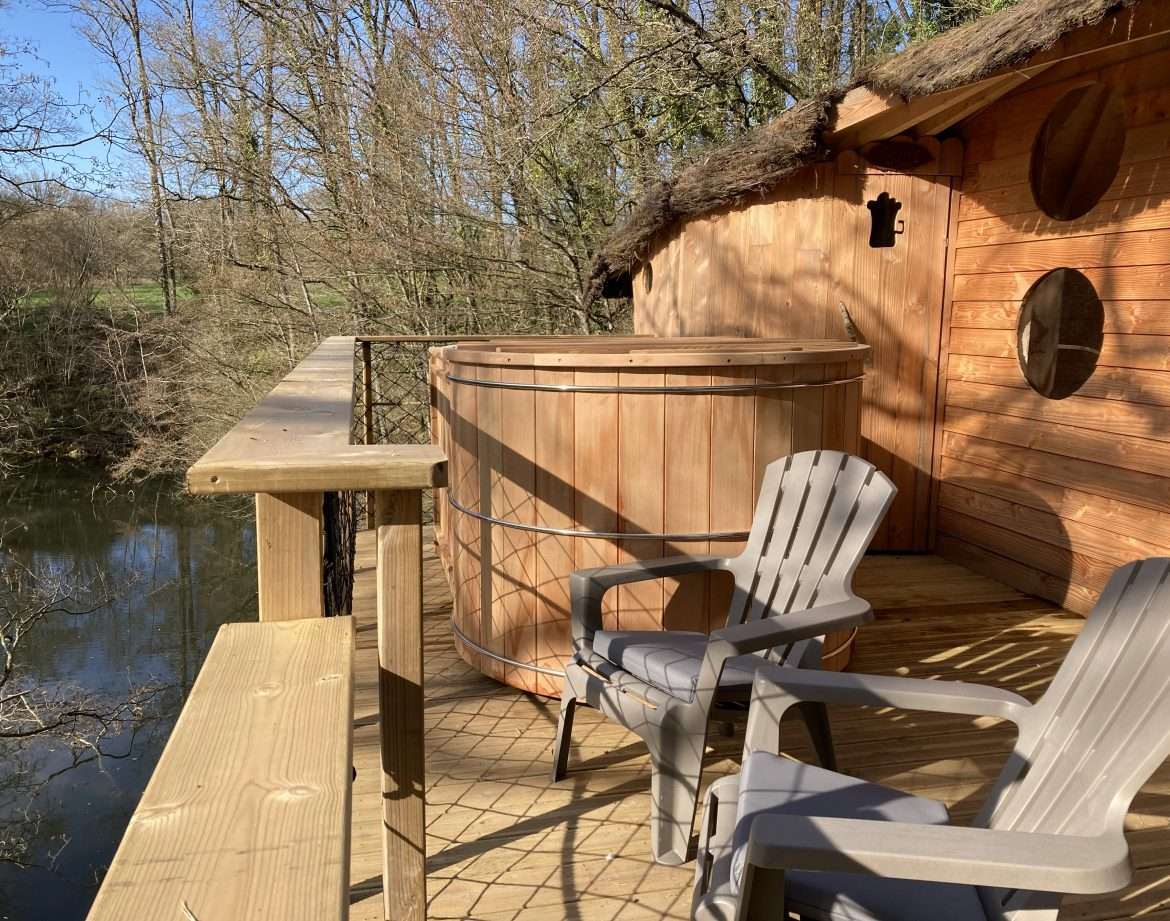 Cabane perchée en bois avec baignoire en bois sur la terrasse, vue sur la rivière.