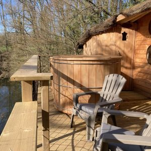 Cabane perchée en bois avec baignoire en bois sur la terrasse, vue sur la rivière.