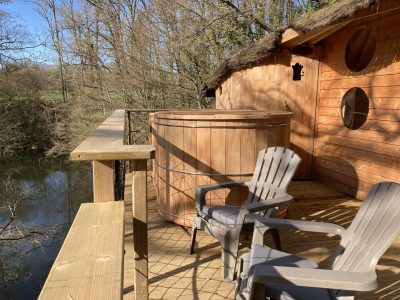 Cabane perchée en bois avec baignoire en bois sur la terrasse, vue sur la rivière.