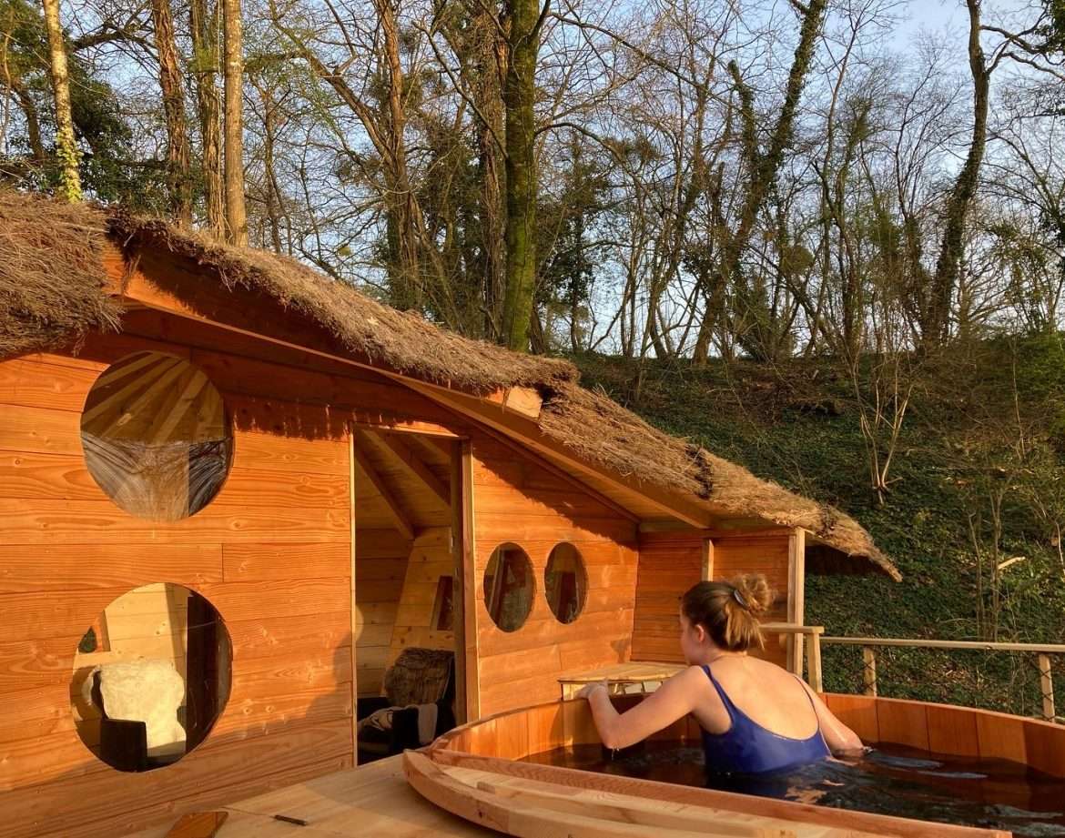 Hébergement insolite en bois avec baignoire extérieure, entouré de verdure.
