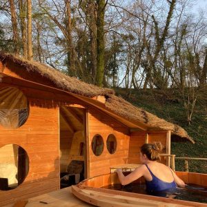 Hébergement insolite en bois avec baignoire extérieure, entouré de verdure.
