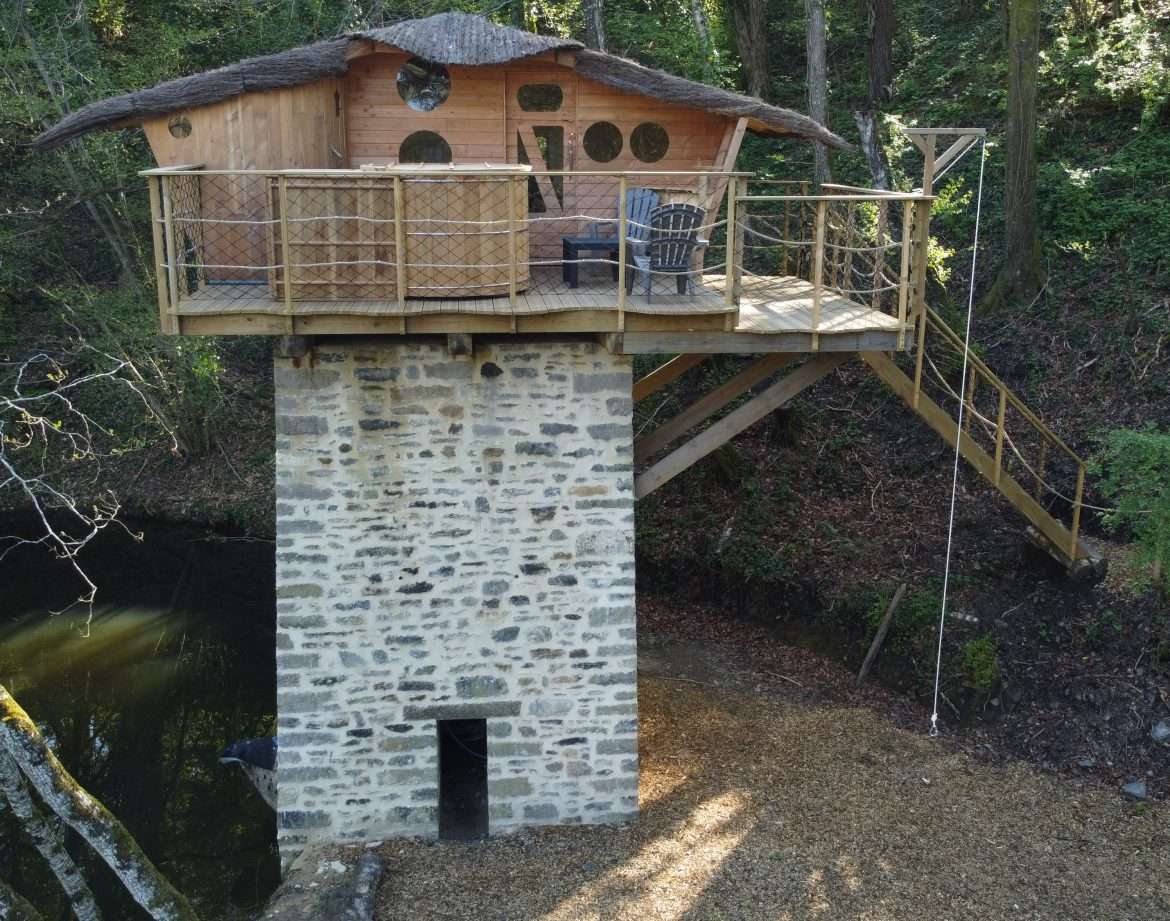 Cabane perchée en bois avec toit de chaume, sur pilotis au bord dun étang.