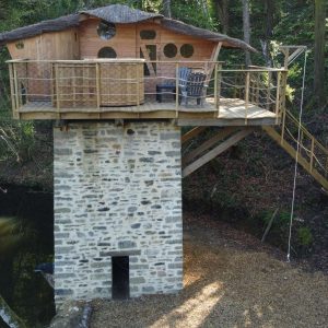 Cabane perchée en bois avec toit de chaume, sur pilotis au bord dun étang.