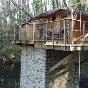 Cabane perchée sur pilotis, entourée de verdure, au bord dune rivière paisible.