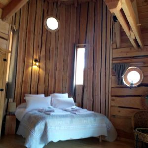Chalet en bois dans les montagnes, avec un lit douillet et des fenêtres rondes.