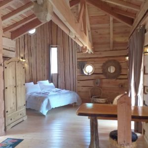 Cabane en bois dans les montagnes, intérieur chaleureux avec lit douillet et lumière naturelle.