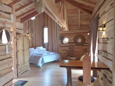 Cabane en bois dans les montagnes, intérieur chaleureux avec lit douillet et lumière naturelle.