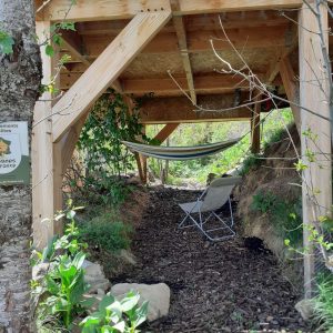 Hébergement insolite en cabane, avec hamac et fauteuil sous les arbres.