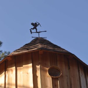 Cabane en bois avec un toit conique et une girouette en métal au sommet.