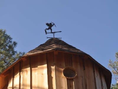 Cabane en bois avec un toit conique et une girouette en métal au sommet.