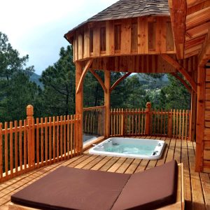 Cabane en bois avec jacuzzi sur une terrasse ensoleillée, vue sur la nature.