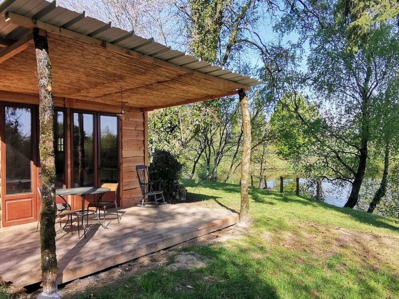 Cabane en bois au bord dun lac, avec terrasse et vue sur la nature verdoyante.