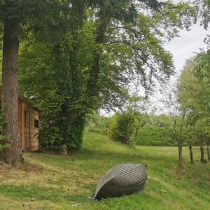 Cabane en bois au bord dune rivière, entourée darbres verdoyants.