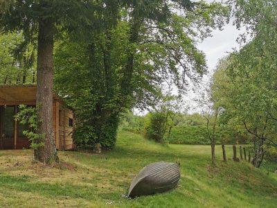 Cabane en bois au bord dune rivière, entourée darbres verdoyants.