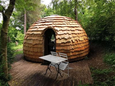 Hébergement insolite en forme de dôme avec un toit en bois, entouré de verdure.