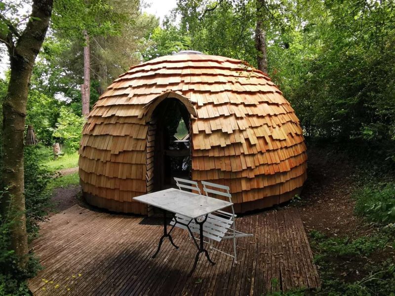 Dôme en bois au cœur de la nature, avec une terrasse et une table extérieure.