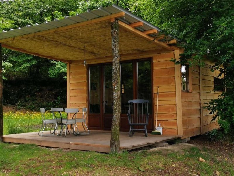Cabane en bois avec terrasse, entourée dune verdure luxuriante.