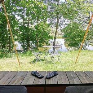 Tente lodge avec vue sur un lac, entourée de verdure et mobilier de jardin.