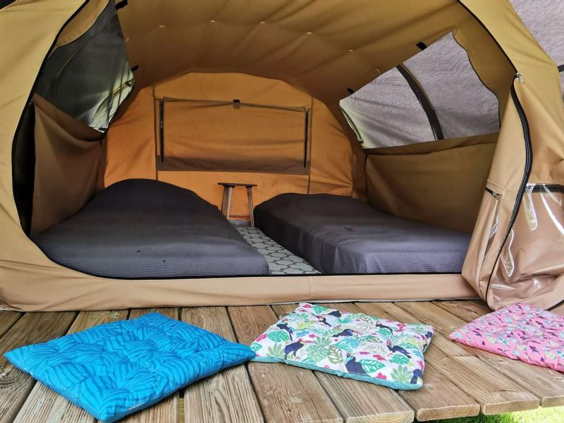 Tente safari spacieuse avec lits confortables et coussins colorés à lentrée.