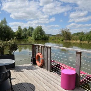 Hébergement insolite en Bourgogne : terrasse sur pilotis avec vue sur leau et mobilier coloré.