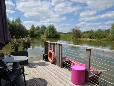 Hébergement insolite en Bourgogne : terrasse sur pilotis avec vue sur leau et mobilier coloré.