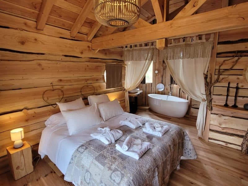 Chalet en bois chaleureux avec lit douillet et baignoire sur pied.
