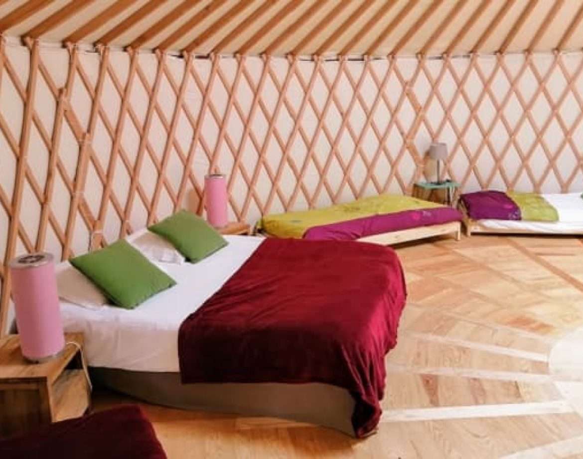 Yourte spacieuse avec lits colorés et parquet en bois, idéale pour un séjour insolite.