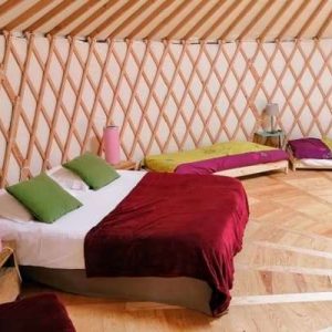 Yourte spacieuse avec lits colorés et parquet en bois, idéale pour un séjour insolite.