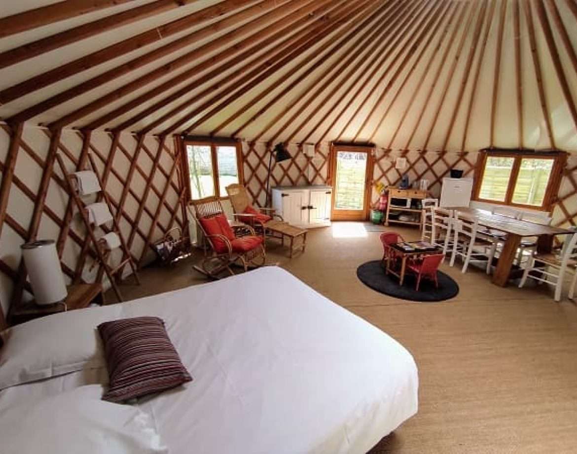 Yourte spacieuse avec intérieur en bois, lit confortable et coin salon accueillant.