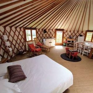 Yourte spacieuse avec intérieur en bois, lit confortable et coin salon accueillant.