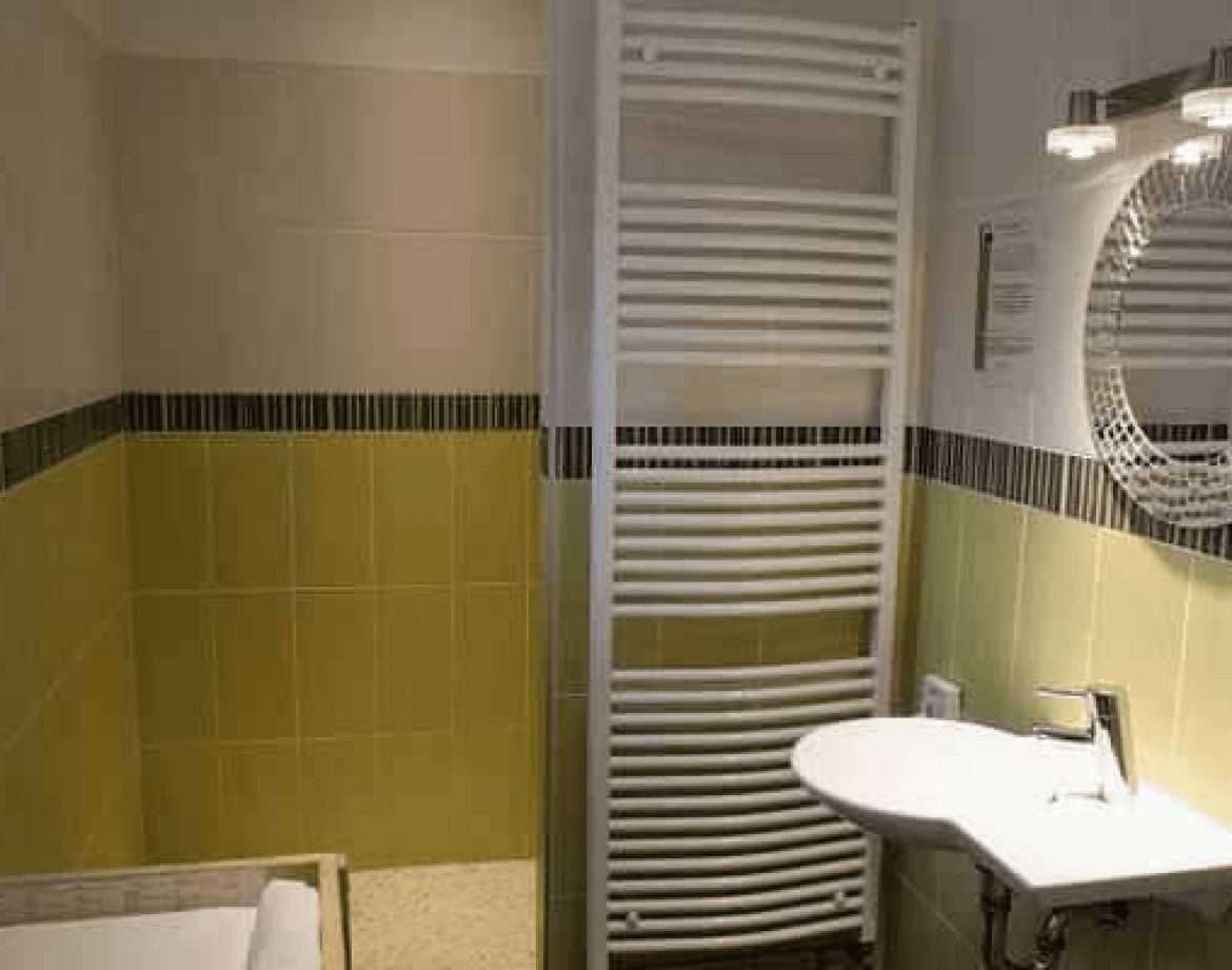 Salle de bain moderne dun hébergement insolite avec carrelage vert et miroir décoratif.