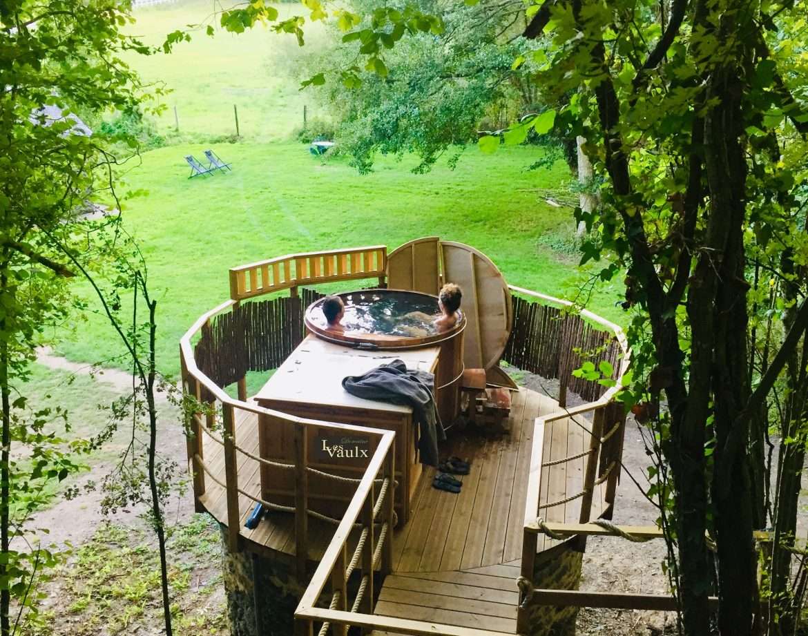 Cabane perchée dans les arbres avec jacuzzi, entourée de verdure apaisante.