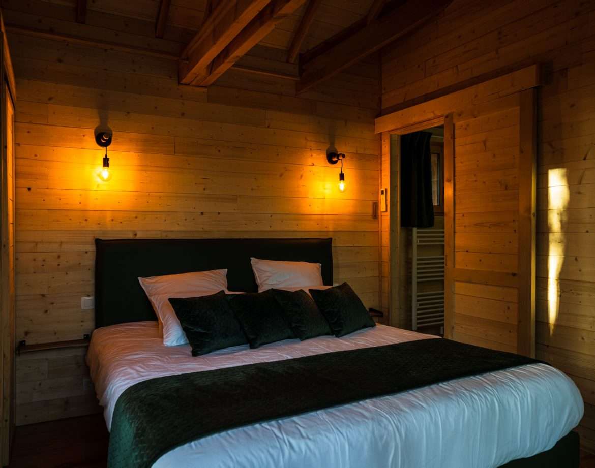 Chalet en bois chaleureux avec lit douillet et éclairage tamisé. Parfait pour un séjour relaxant.