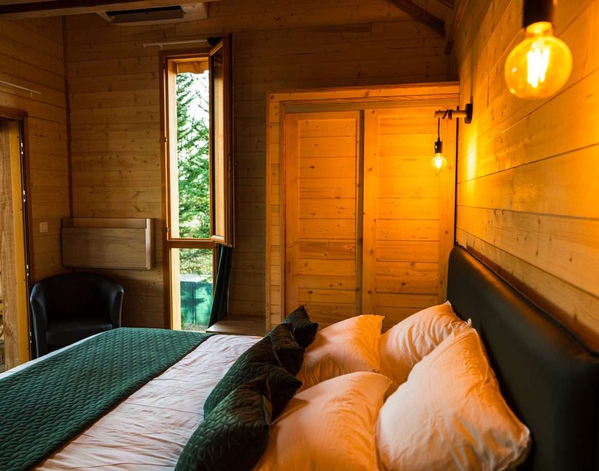 Chalet en bois chaleureux avec lit douillet et lumière tamisée. Vue sur la nature.