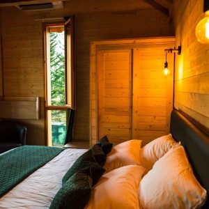 Chalet en bois chaleureux avec lit douillet et lumière tamisée. Vue sur la nature.