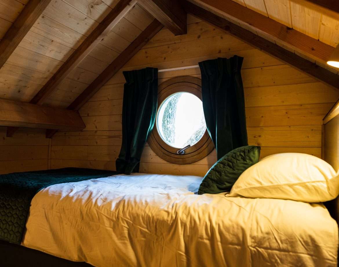 Chalet en bois avec fenêtre ronde, lit douillet sous un plafond en pente.