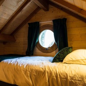 Chalet en bois avec fenêtre ronde, lit douillet sous un plafond en pente.