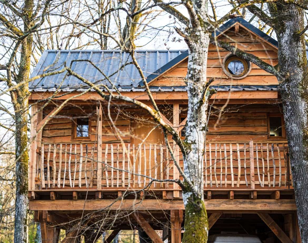 Cabane perchée en bois, nichée entre les arbres, avec un balcon accueillant.